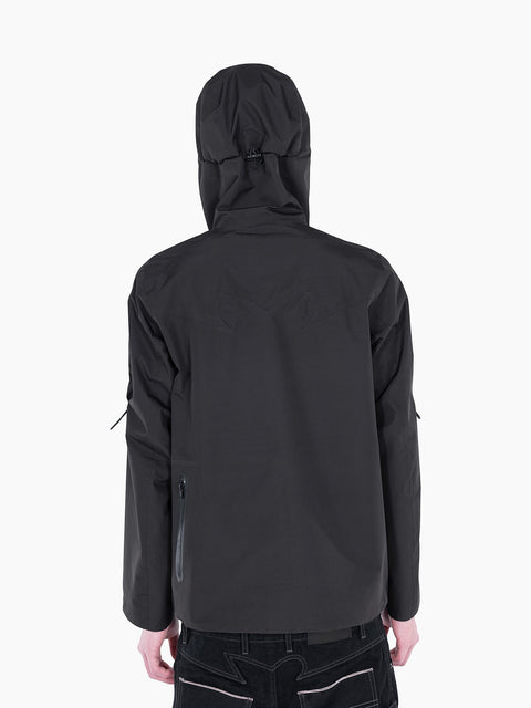 Back view of VAIN black waterproof shell jacket with signature heart-shaped yoke, hood, and taped seams on a model.
